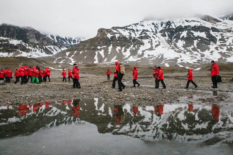 Ein Gruppe von Gästen der Kreuzfahrt wandert in Spitzbergen vor schneebedeckten Bergen